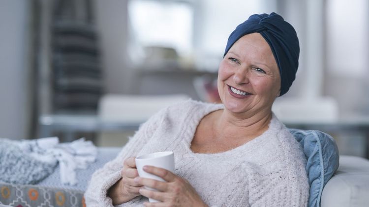 Eine lächelnde Frau mit Teetasse und Kopftuch.