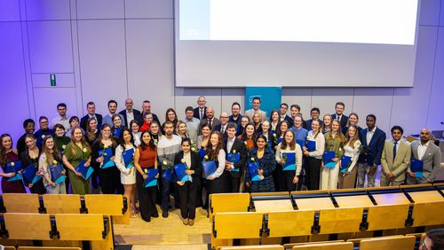 Gruppenfoto im Hörsaal. Hinter den Personen ist eine Präsentation zu erahnen. Im Vordergrund die typische Hörsaalbestuhlung.