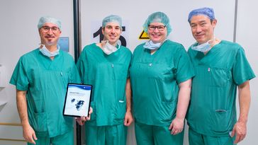 Vier Personen mit OP-Kleidung posieren für ein Foto. Einer hält ein Zertifikat.