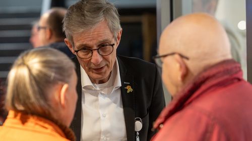 Griesinger unterhält sich mit einer Besucherin und einem Besucher, die mit dem Rücken zur Kamera stehen.