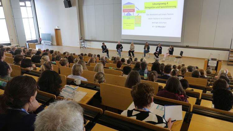 Bild vom Hörsaal von hinten. Vorn ist eine Präsentation zu erahnen. Der Saal ist gut gefüllt.