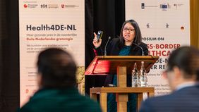 Frau spricht am Pult vor Publikum. 