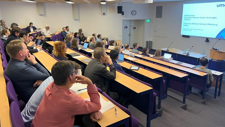 In einem Hörsaal sitzen mehrere Menschen und hören dem Redner zu.