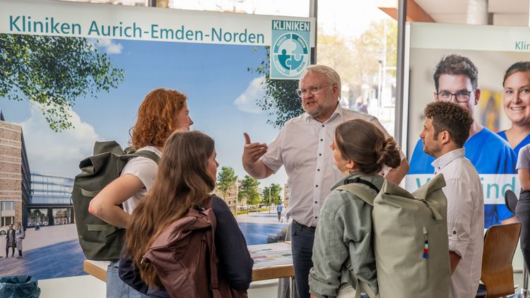 Studierende unterhalten sich mit einem Mann vor einem Banner der Kliniken Aurich-Emden-Norden.