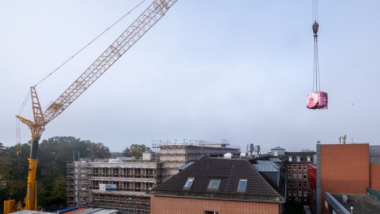 MRT-Gerät hängt am Haken eines Krans über den Dächern des Klinikums.