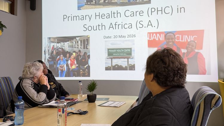Frauen an einem Besprechungstisch schauen gemeinsam auf eine Präsentation mit dem Titel "Primary Health Care in South Africa"