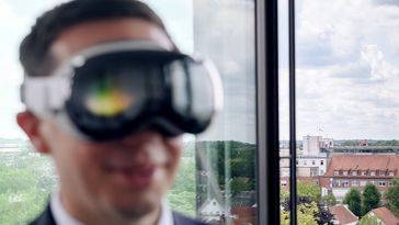 Vorn unscharf Mohrs mit VR-Brille, im Hintergrund ist klein ein Hubschrauber auf einem Dach zu erkennen.