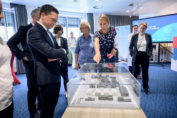 Mohrs betrachtet einen 3D-Lageplan des Klinikums aus Modellen. Eine Frau deutet auf eines der Modellgebäude.