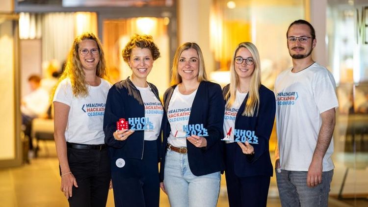 Fünf Personen mit Healthcare-Hackathon-T-Shirt lächeln in die Kamera. Drei von ihnen halten einen Award mit dem Schriftzug HHOL2025 in den Händen.