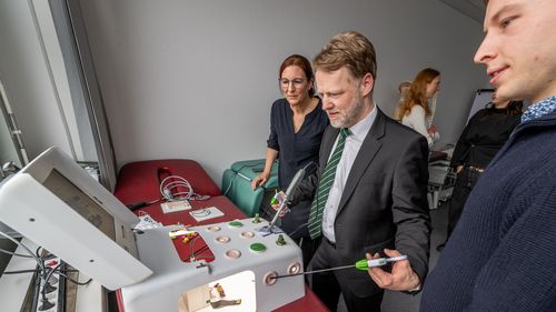 Heeremann hält zwei Griffe in der Hand, an denen etwa 40 Zentimeter lange Stäbe befestigt sind, die rechts und link in einen eckigen Kasten führen, der vor ihm steht. Auf dem Kasten ist ein kleiner Monitor, mit dem er beobachten kann, was im Kasten passiert.
