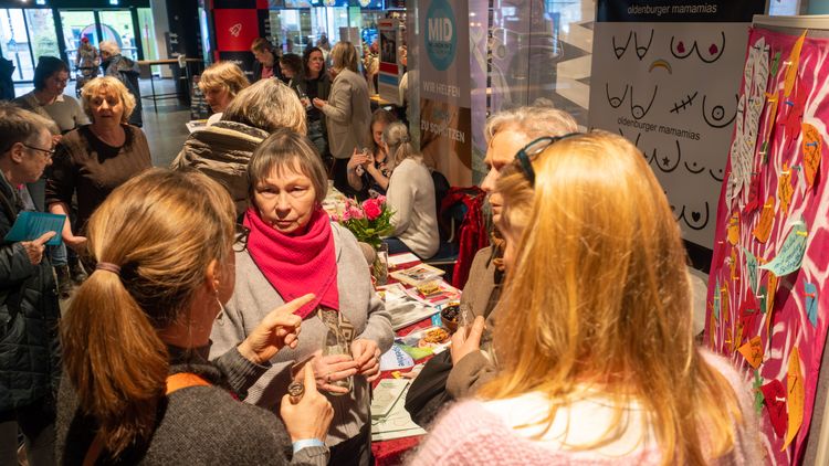Mehrere Personen unterhalten sich an einem Informationsstand zum Thema Brustkrebs, im Hintergrund sind weitere Stände zu erkennen.