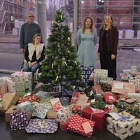 Die genannten Personen um einen Weihnachtsbaum mit Kerzen. Vor ihnen liegen viele verpackte Geschenke.