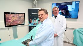 Minister Philippi seht an einem OP-Tisch und führt zwei OP-Instrumente, die zu einem Simulator gehöre. Auf einem Monitor ist die grafische Darstellung des Bauchraums zu sehen, in dem die simulierte OP stattfindet. Neben Philippi steht Dirk Weyhe.