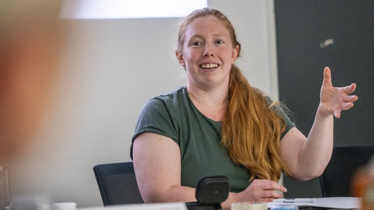 Mira Richts hat lange rotblonde Haare, die zum Zopf gebunden über ihrer Schulter liegen. Sie trägt ein grünes T-Shirt. Während sie spricht, gestikuliert sie mit der linken Hand.