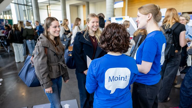 Zwei Frauen mit blauem T-Shirt, auf dem "Moin" steht, beraten zwei junge Frauen. 