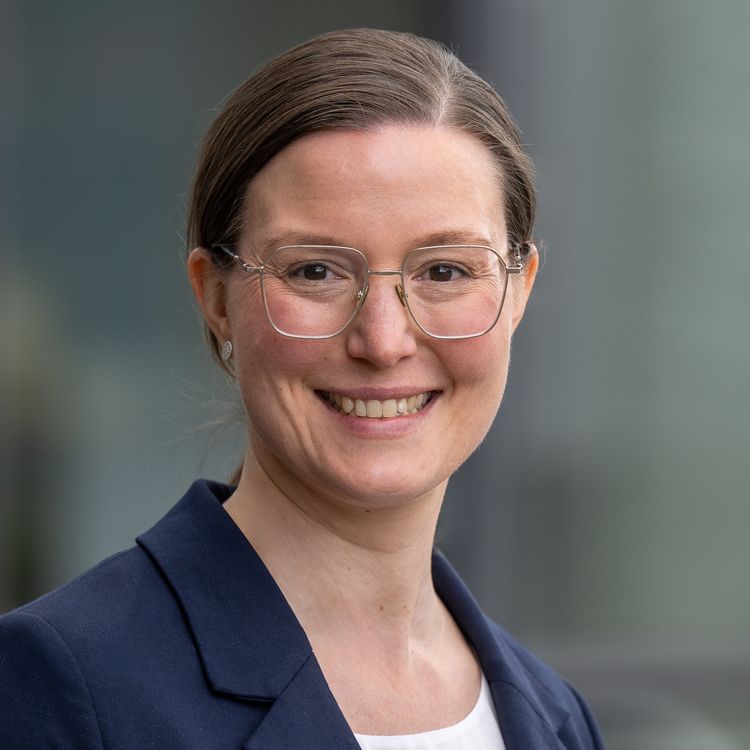 Porträt von Hannah Maier: Sie hat dunkle Haare, zusammengebunden, trägt ein weißes Shirt und einen blauen Blazer und lächelt in die Kamera.