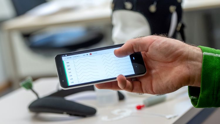 Auf einem Smartphone-Display sind wellenförmige EEG-Messdaten zu sehen.