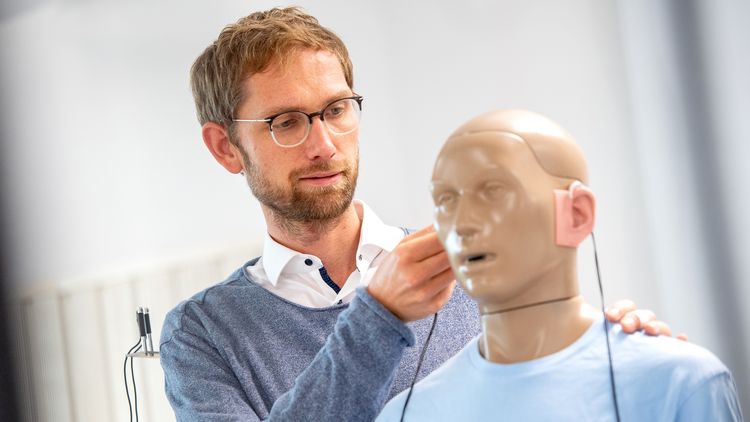 Kai Siedenburg im Hörlabor mit einer schaufensterartigen Puppe, die Hörgeräte trägt.