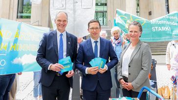 Die drei Personen stehen vor dem Landtag in Hannover und lächeln in die Kamera. Mohrs und Bruder haben Postkarten der Unterschriftenaktion in der Hand.