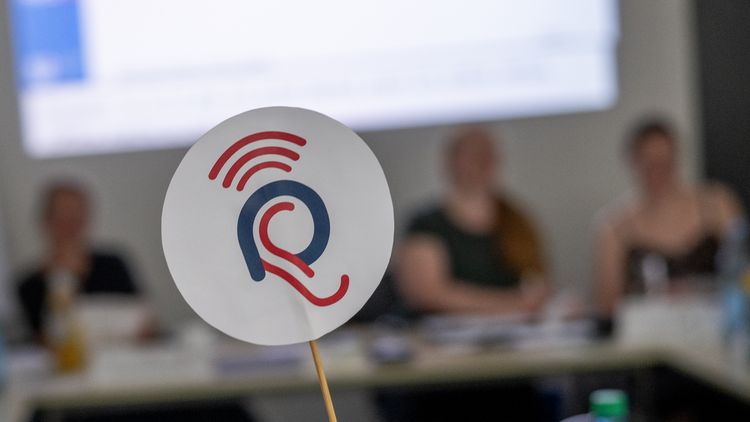 Im Hintergrund ist ein unscharfer Seminarraum zu erkennen, im Vordergrun ist eine kleine Kelle aus Papier mit HEARAZ-Logo